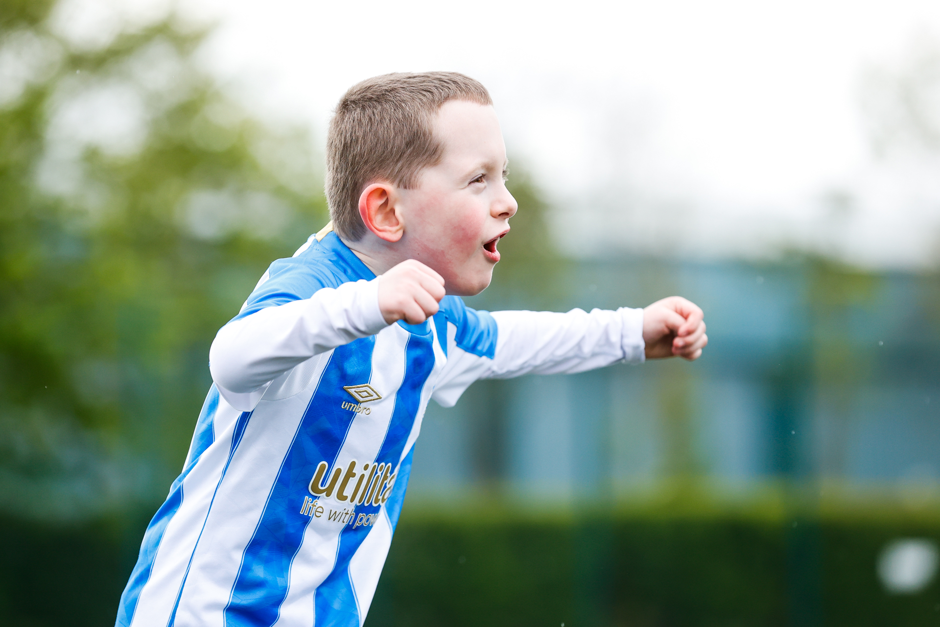 A white young boy wearing a Huddersfield Town shirt celebrating a goal with his arms held out wide