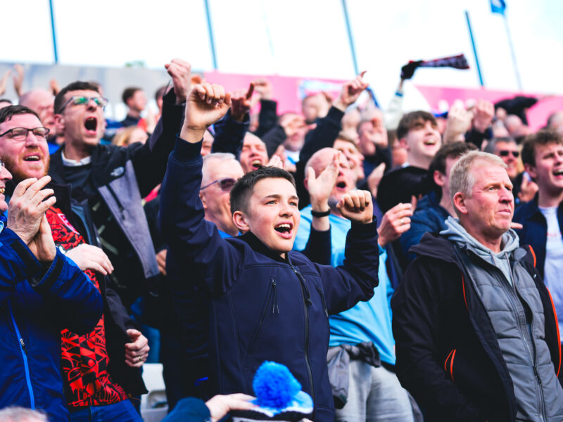 Male Huddersfield Town fans celebrating with their hands in the air in the stands as Huddersfield score away to Stockport County