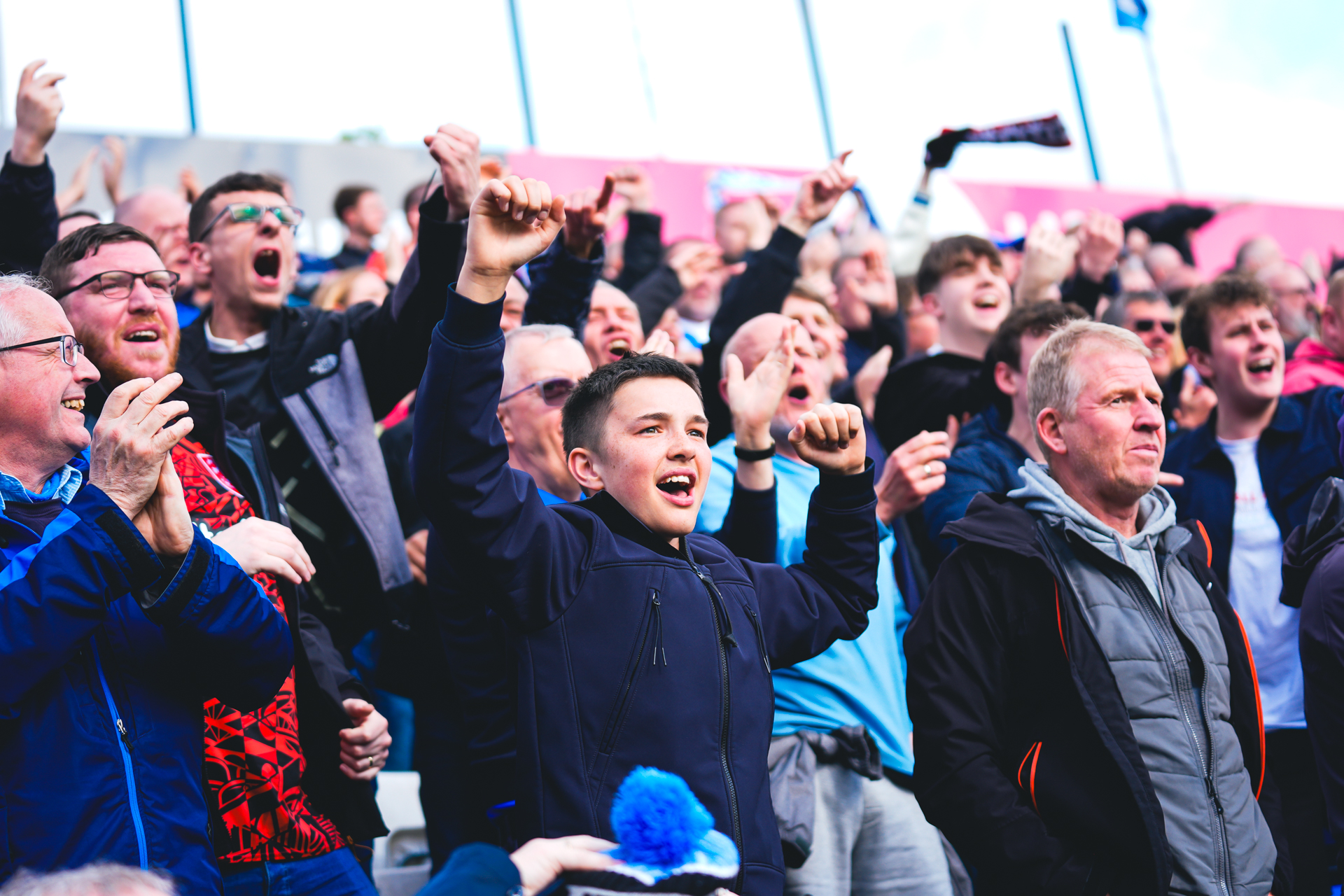 Male Huddersfield Town fans celebrating with their hands in the air in the stands as Huddersfield score away to Stockport County